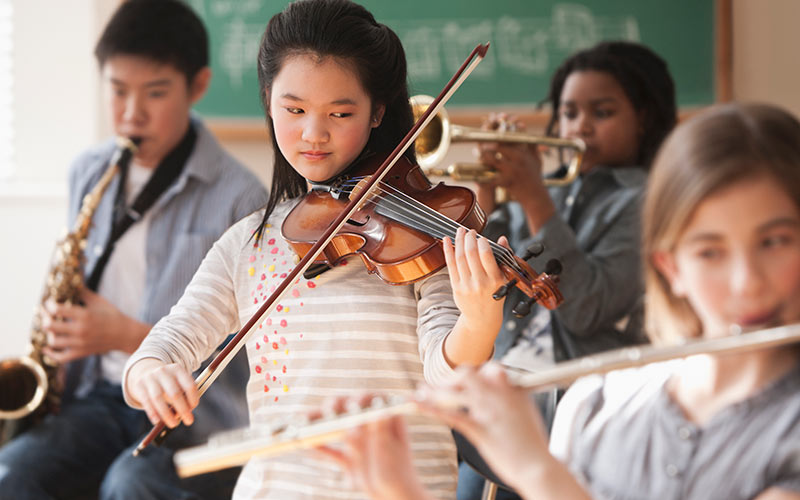 A young girl plays violin in a class with other children.